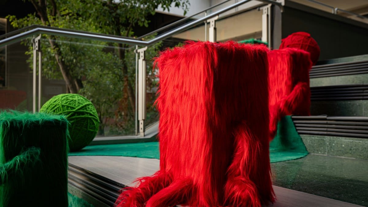 Bright red furry sculptural installation with green organic forms — expressive design