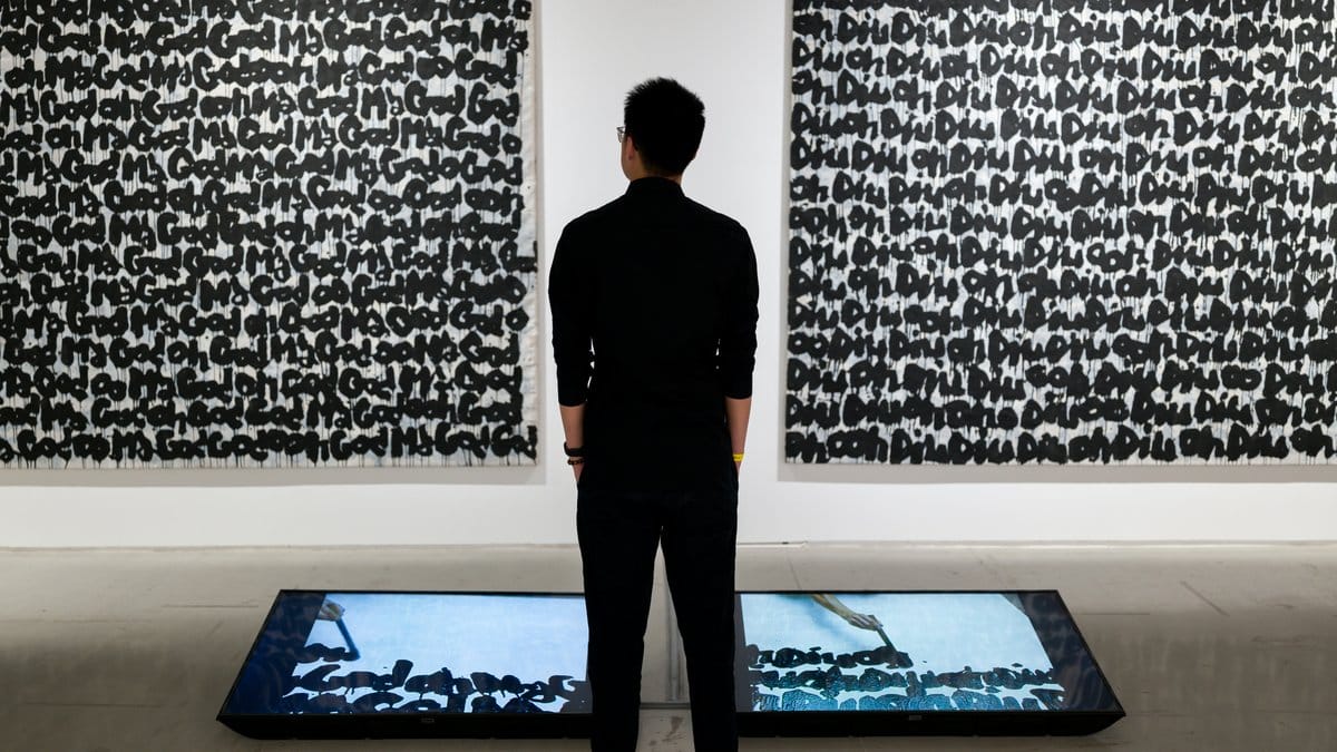 Person standing before large text-based graffiti paintings in a gallery — Basquiat contemporary art