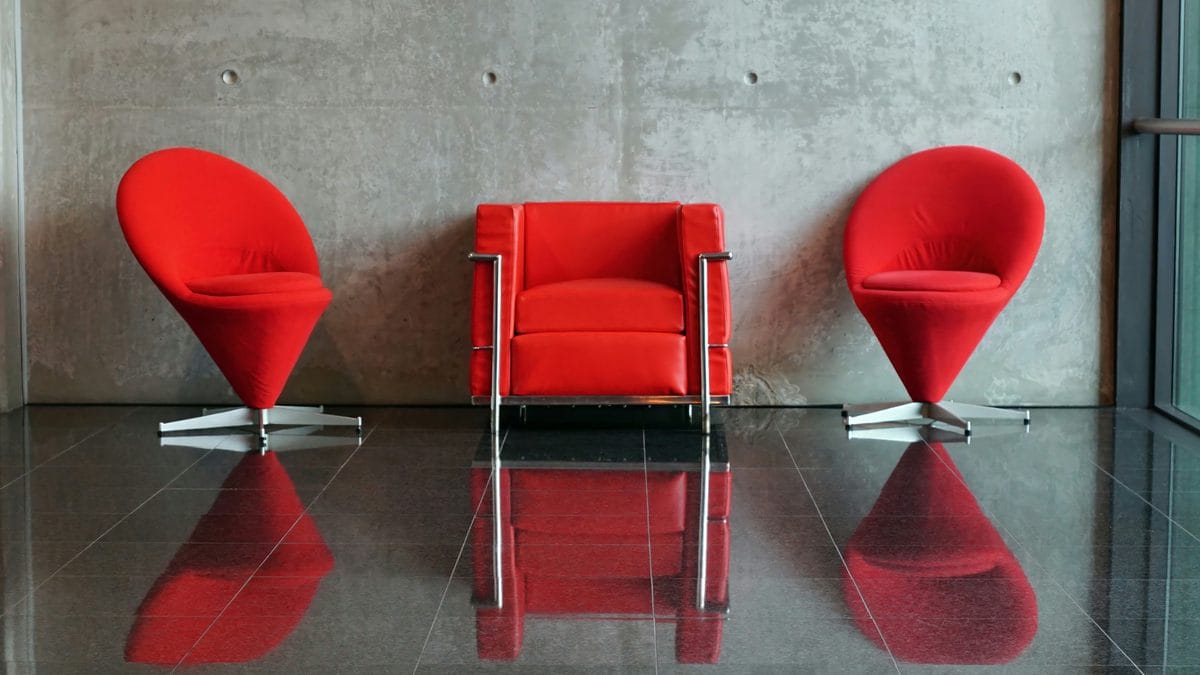 Red designer chairs including Panton Cone chairs and Le Corbusier LC2 armchair against a concrete wall