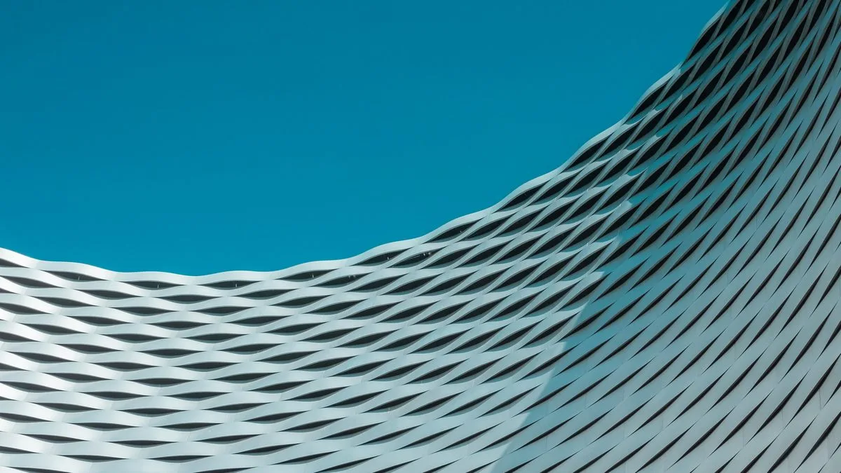 Curved white modern building facade with diamond lattice pattern against a teal sky