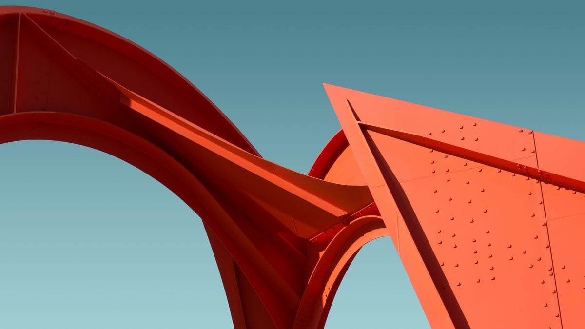 Red Calder-style steel sculpture with curved arches and riveted panels against a teal sky